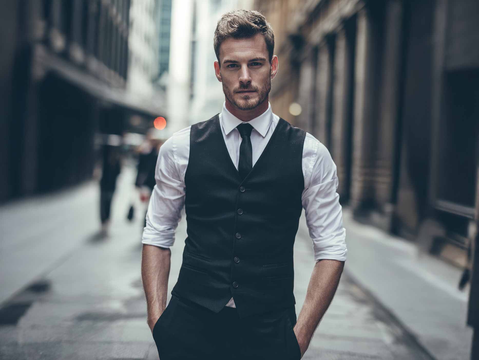 Ein Mann trägt ein weißes Hemd, dazu eine schwarze Krawatte und eine enganliegende schwarze Anzugweste.