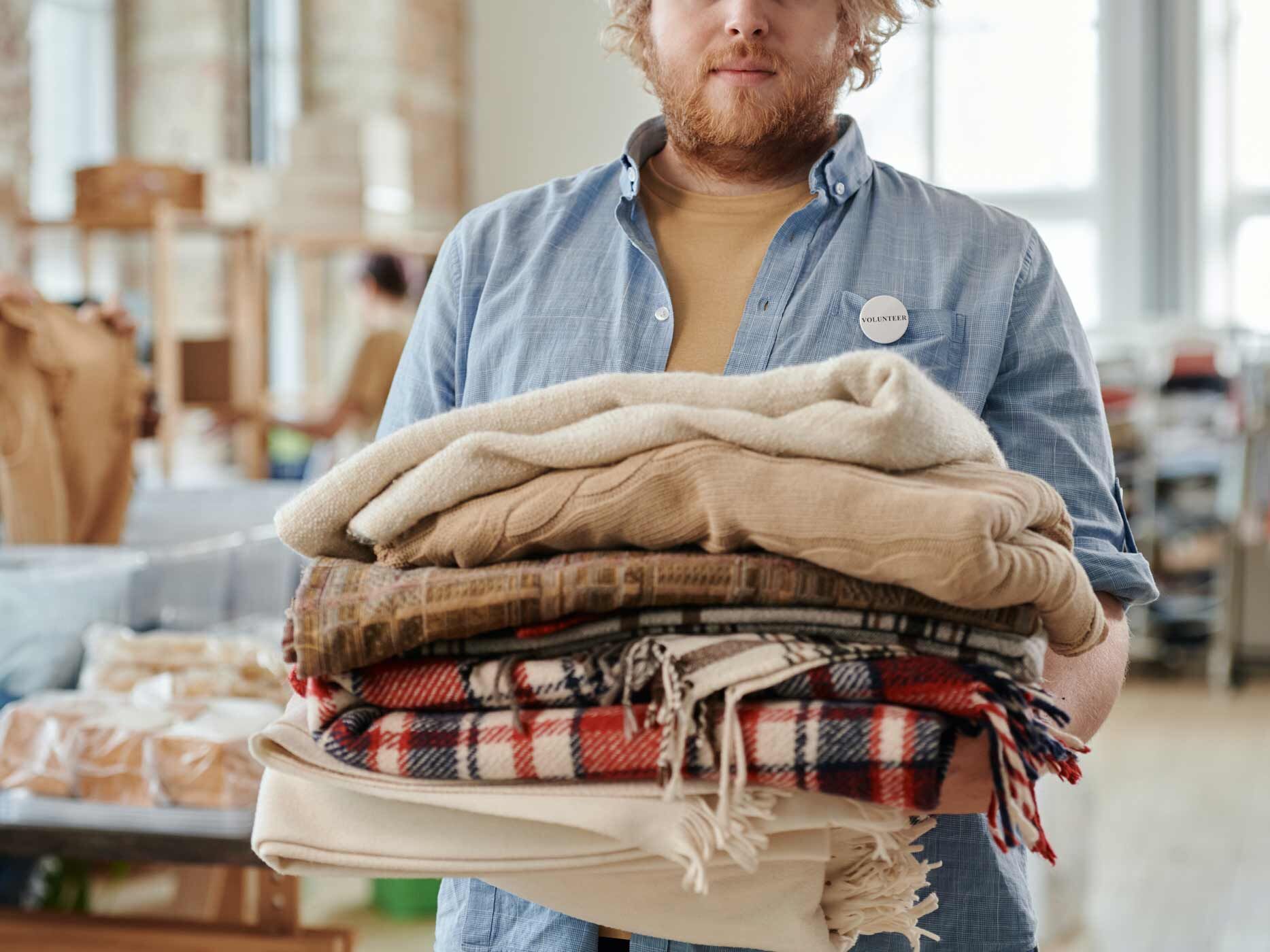 Mann in einer Kleiderkammer hält Stapel mit Kleidung in den Armen