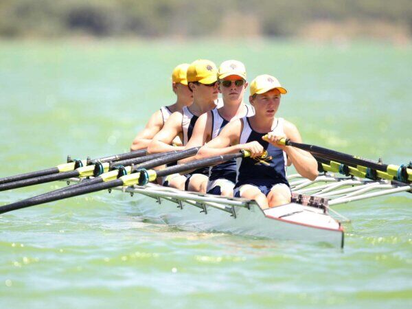 Vier Jungs sitzen in einem Ruderboot auf dem Wasser.