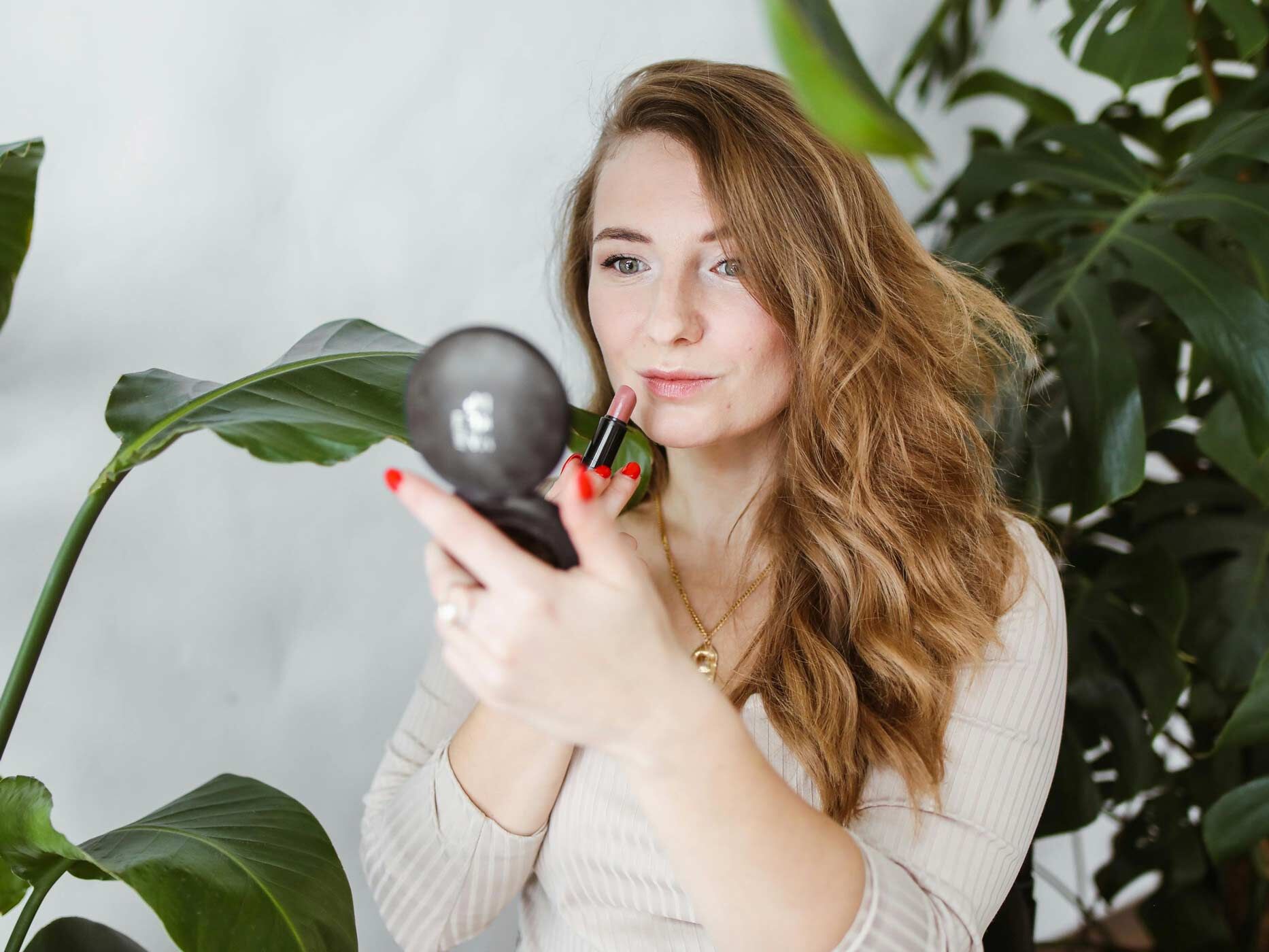 Eine Frau hält einen kleinen Kosmetikspiegel in der Hand und trägt sich mit der anderen Lippenstift auf.