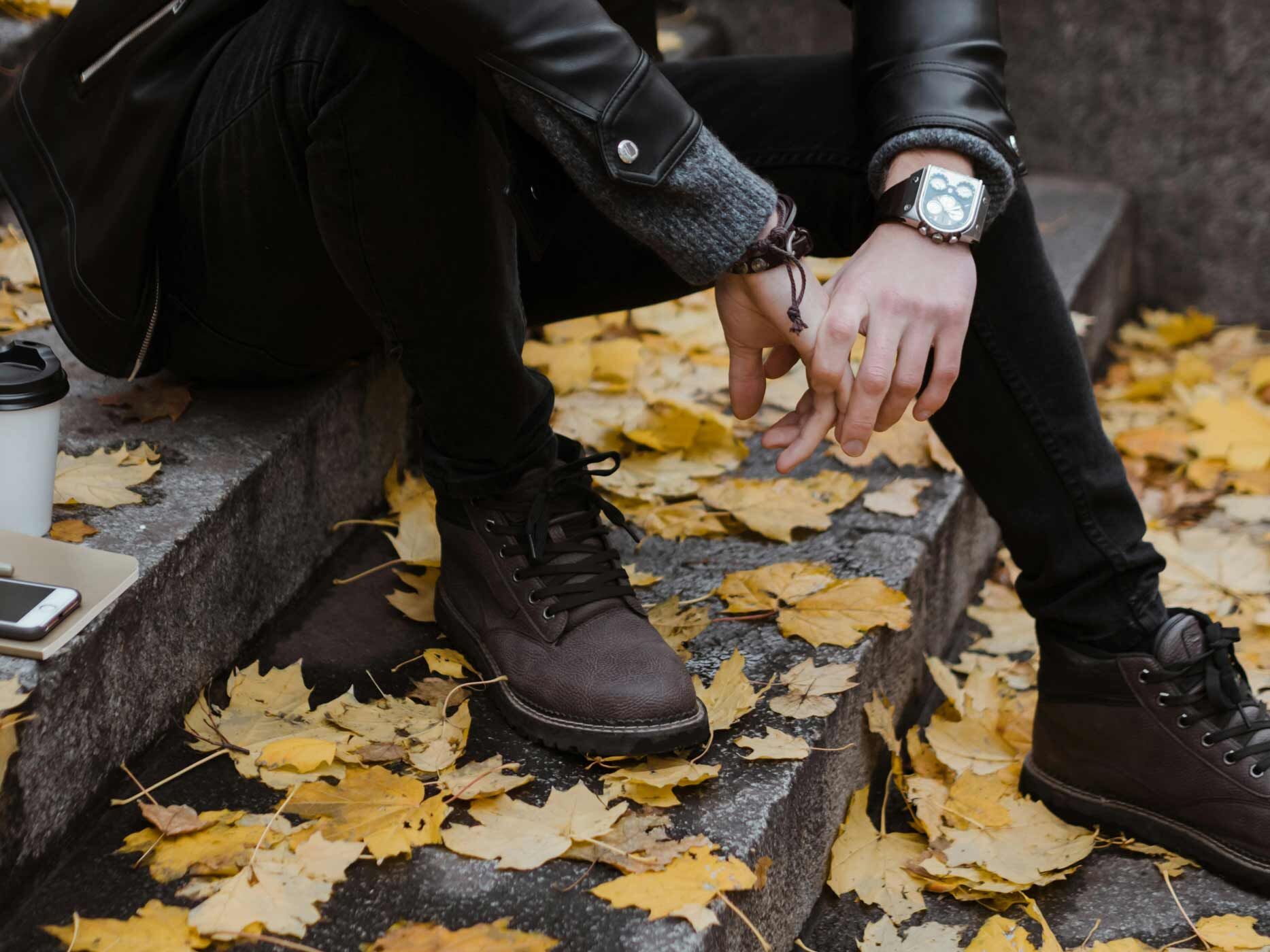 Ausschnitt von einem Mann, der l&auml;ssig auf einer Steintreppe sitzt und schwarze Jeans und schwarze Lederjacke tr&auml;gt.