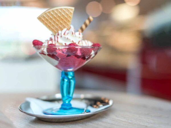 Ein Eisbecher mit Himbeeren und Waffel stehen auf dem Tisch.