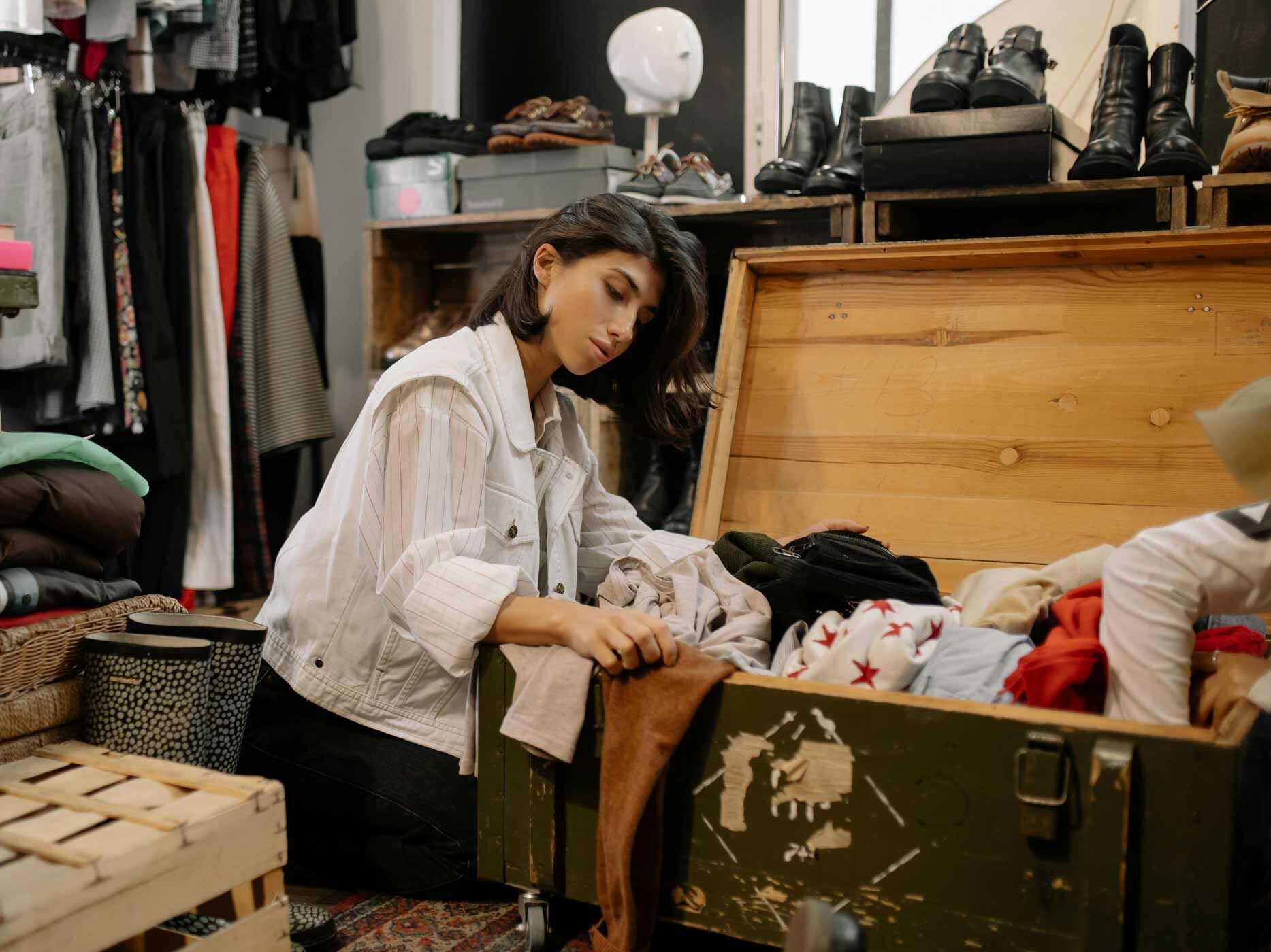 Eine Frau stöbert in einer Kiste mit Second Hand Mode.