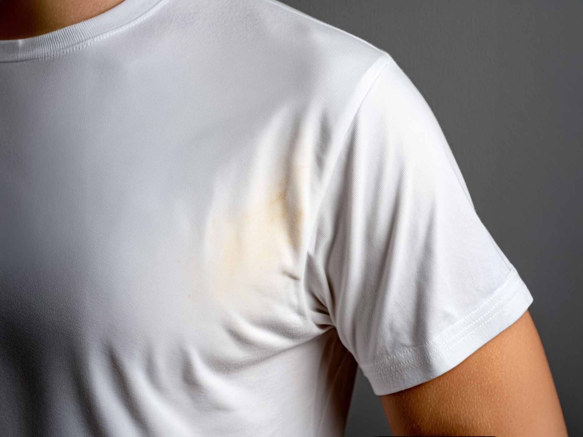 Ein Mann trägt ein weißes T-Shirt, auf dem im Achselbereich gelbe Flecken sind.