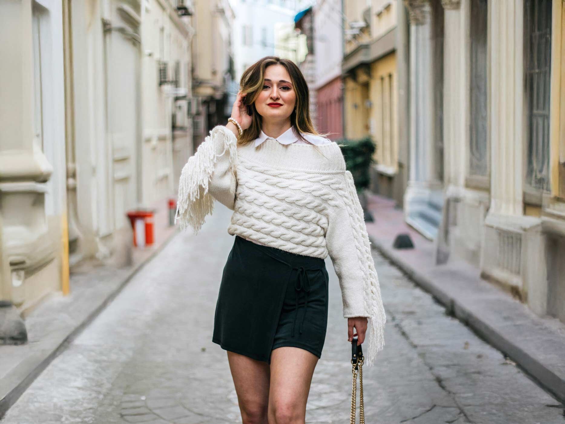 Eine Frau läuft durch eine Straße. Sie trägt einen schwarzen Rock, der mit weißer Bluse und Pullover gestylt ist.