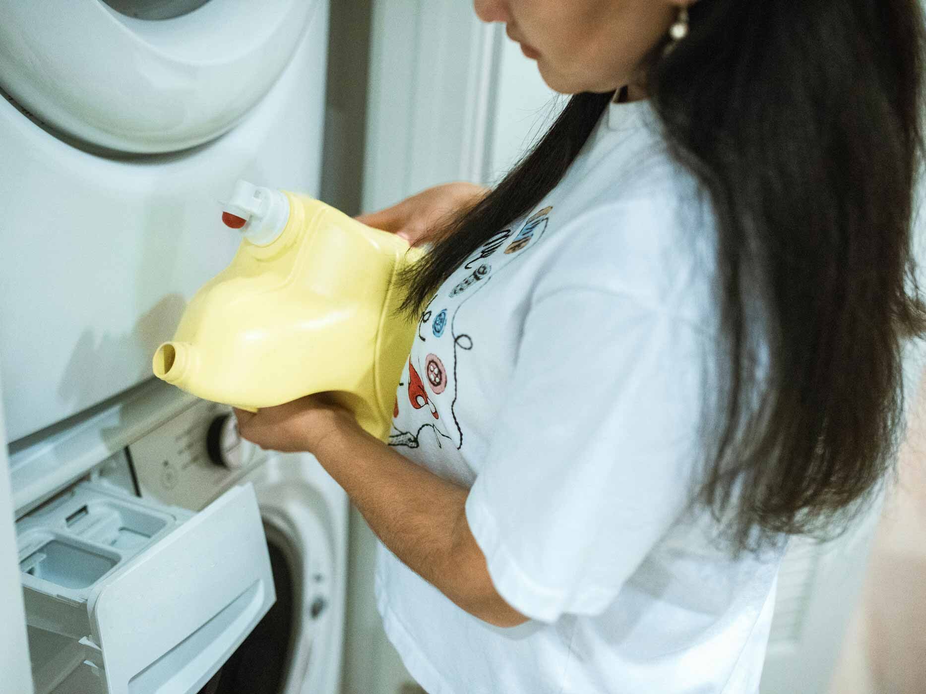 Eine Frau kippt flüssiges Waschmittel in ihre Waschmaschine.