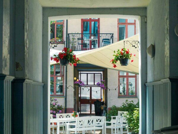 Aussicht aus einer Tür heraus auf einen Innenhof, der mit weißen Bänken und Tischen geschmückt ist.