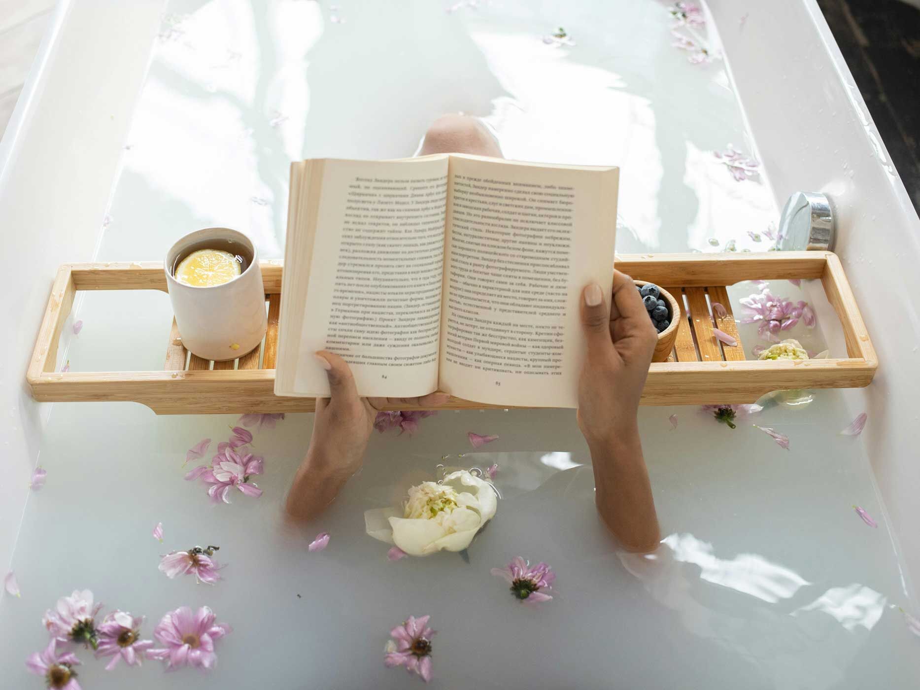 Frau liegt mit Blumen im Wasser in der Badewanne und liest ein Buch