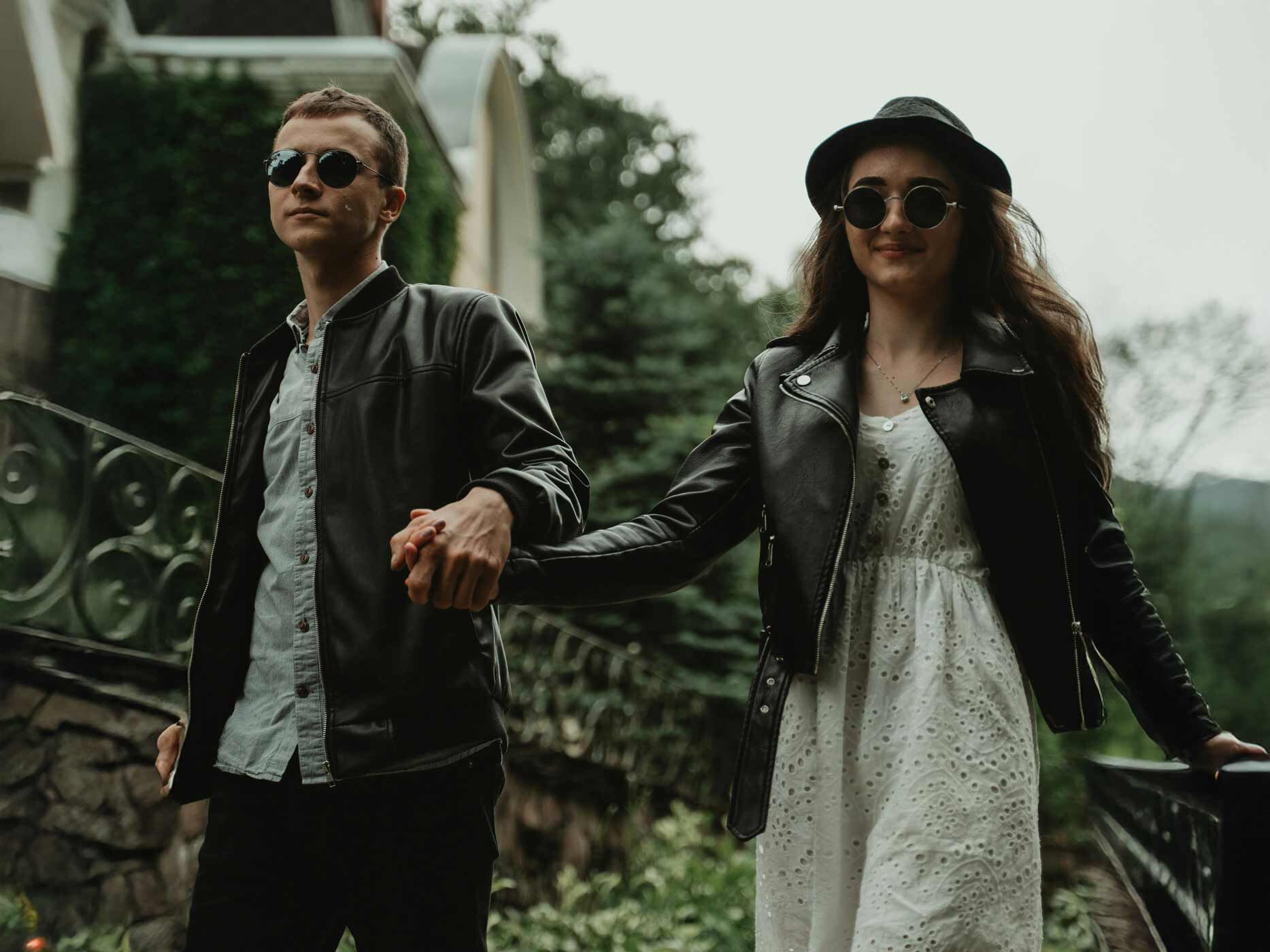 Eine Frau trägt ein kurzes weißes Sommerkleid, welches ein verspieltes Punktemuster zeigt. Darüber trägt sie eine schwarze Lederjacke, eine schwarze Sonnenbrille und einen große schwarzen Hut.